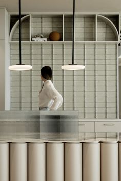 a woman standing in front of a counter with three lamps hanging from it's ceiling