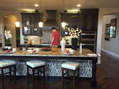 a woman standing at the center of a kitchen island in front of a stove top oven