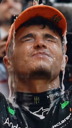 a man is drinking water from a faucet in front of his face while wearing an orange hat