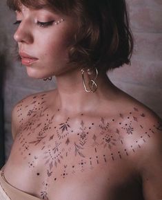 a woman with tattoos on her chest looking down at the camera while wearing gold hoop earrings