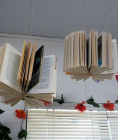 an open book hanging from the ceiling with holly garland around it and two opened books above them