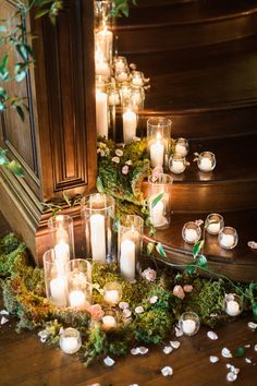 many candles are lit on the ground next to some flowers and greenery in glass vases