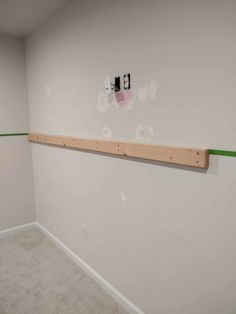 an empty room with white walls and green tape on the wall next to a wooden shelf