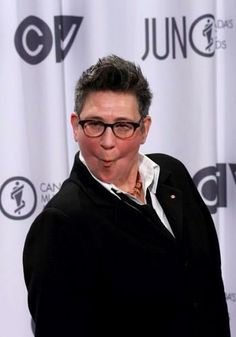 a man with glasses standing in front of a red carpet and white curtained backdrop