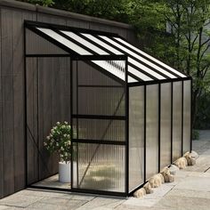 a small black greenhouse sitting on top of a stone patio next to a wooden fence