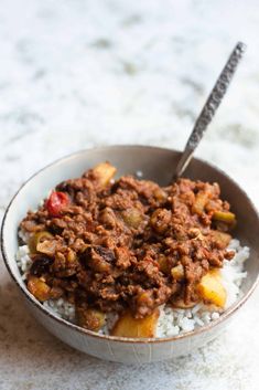 a bowl filled with rice and meat on top of a white countertop next to a spoon