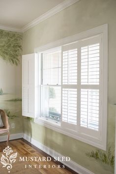 a chair sitting in front of a window next to a wall with trees painted on it