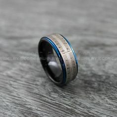 a wedding band with blue and silver inlays sits on top of a wooden table