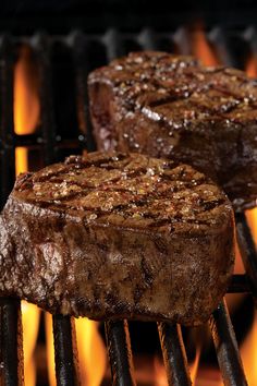 two steaks cooking on the grill with flames