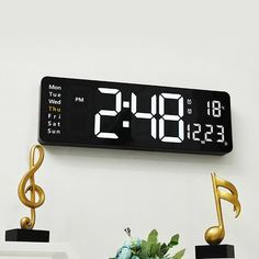 a digital clock with musical notes on the front and back sides next to a potted plant