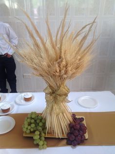 a table topped with grapes and cupcakes next to a vase filled with wheat