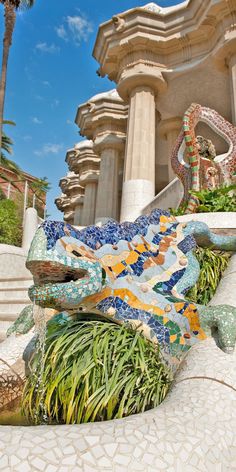 a statue of a lizard is in front of a building with stairs and plants on the ground