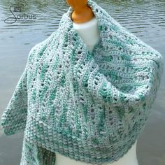 a knitted shawl is sitting on a mannequin in front of a body of water