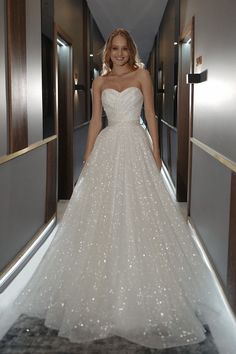 a woman in a white wedding dress is walking down the hall with her hands on her hips