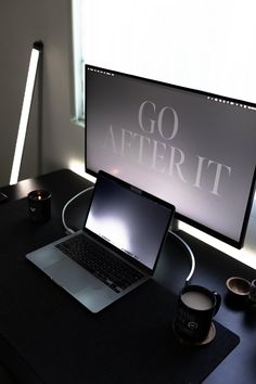 a laptop computer sitting on top of a desk next to a monitor and coffee mug