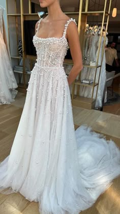 a woman standing in front of a dress on display at a bridal shop wearing a white gown with sequins and beading