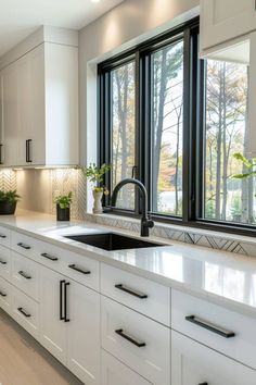 a kitchen with white cabinets and counter tops next to a window that has trees outside