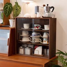 a wooden cabinet filled with lots of coffee cups and saucers next to a potted plant