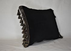 a black pillow with gold tassels on the bottom and sides, against a white background