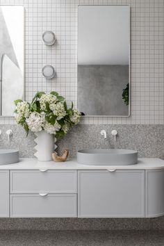 a bathroom with two sinks, mirrors and flowers in the vase on the counter top