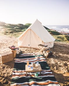 a tent is set up on the beach with picnic food and drinks in front of it