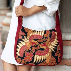 Sawunggaling refers to a traditional Javanese pattern inspired by the King's favorite rooster, a symbol of the nation's power and beauty. Featured in many palaces, this fascinating image is now present in Wahyu Sulistiani's cotton shoulder bag, crafted using batik techniques. The accessory comes in a red hue, with golden-toned plastic beads adding a luxurious touch. On top of that, the design has a zippered closure, a black cotton lining and an interior pocket. Cheap Handmade Traditional Shoulder Bag, Shoulder Bag Outfit, Travel Bag Set, Batik Art, Honeymoon Gifts, Face Mask Set, Buy Bead, Beaded Handbag, Travel Cosmetic Bags