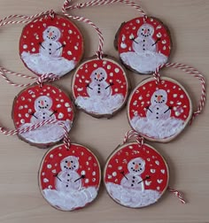 six decorated cookies with snowmen in red and white designs hanging from twine strings