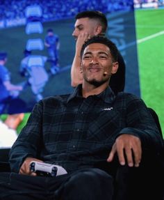 two men sitting next to each other in front of a tv screen with a soccer game on it