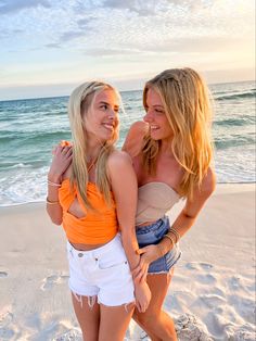 two beautiful young women standing next to each other on a sandy beach near the ocean