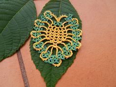 a green leaf with a yellow and blue brooch sitting on it's side