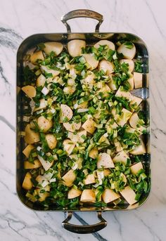 a pan filled with potatoes and greens on top of a marble countertop next to a silver spoon