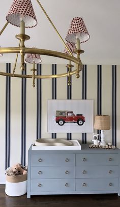 a baby's room with blue dresser and striped wallpaper, including a red car