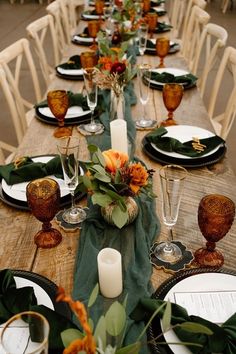 a long table set with place settings and flowers on the centerpieces is surrounded by greenery