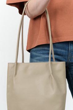 The Frances Bag is an elegantly designed shoulder bag featuring a soft form and an oval base, complemented by two rolled shoulder straps adorned with pinched details. Made from unlined vegetable-tanned semi-aniline cowhide, it offers a luxurious yet durable finish. This versatile accessory is ideal for everyday use, providing ample space to accommodate all your daily essentials with style and sophistication. Beige Rectangular Shoulder Bag With Rolled Handles, Rectangular Beige Shoulder Bag With Rolled Handles, Classic Beige Square Bucket Bag, Classic Square Hobo Bag In Soft Leather, Classic Soft Leather Square Hobo Bag, Beige Leather Baguette Bag For Everyday, Chic Rectangular Shoulder Bag With Rolled Handles, Classic Baguette Bag With Leather Handles For Daily Use, Modern Rectangular Shoulder Bag With Rolled Handles