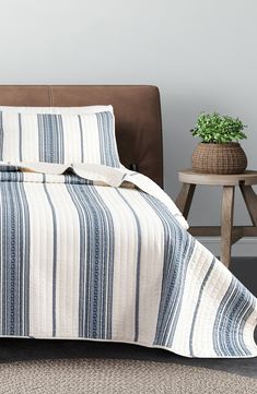 a bed with blue and white striped bedspread next to a brown leather headboard