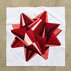 a red and white quilted star on top of a piece of paper that is laying on the ground