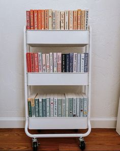 there is a book shelf with many books on the top and two wheels below it