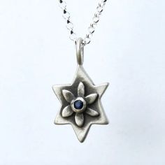 This sterling Star of David necklace departs from convention by featuring a flower at its center that cradles a set stone of your choice. Patina brings out the details of the design and helps make it a striking gift for a Bat Mitzvah or for any age. It hangs on a 16" fine gauge sterling rolo chain (optional longer chain length available through the drop-down menu below). Charm is 3/4". Handmade in the USA by Emily Rosenfeld. Please allow 3-5 business days to ship. Shop our full collection of Jew Sterling Silver Star Gemstone Jewelry, Spiritual Star-shaped Gemstone Jewelry, Spiritual Oxidized Flower Pendant Jewelry, Silver Star Of David Necklace With Gemstone, Spiritual Star Charm Pendant Jewelry, Silver Star Of David Birthstone Jewelry, Spiritual Silver Jewelry With Star Charm, Silver Star Of David Jewelry With Birthstone, Silver Star Necklaces With Birthstone