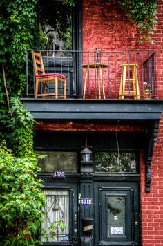 two wooden chairs sitting on top of a balcony next to a red brick building with green plants