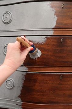 a person painting a chest of drawers with gray and white paint on the top part