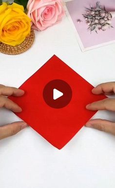 two hands holding up a red piece of paper with the video below it on a table