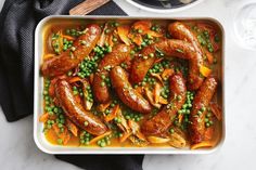 a white dish filled with sausages and peas