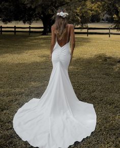 a woman in a white dress is walking through the grass with her back to the camera