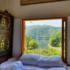 an unmade bed sitting in front of a window overlooking a mountain valley and lake