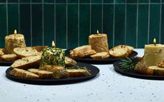 three black plates with slices of bread on them and lit candles in the middle one