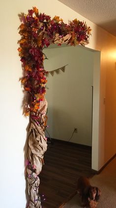 a dog is standing in front of a decorated arch with leaves and ribbons on it