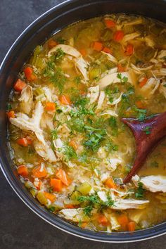 a pot filled with chicken and carrots on top of a table next to a wooden spoon