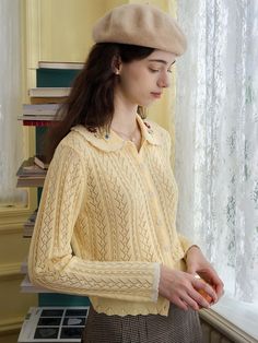 a woman standing in front of a window with a hat on her head and wearing a yellow sweater