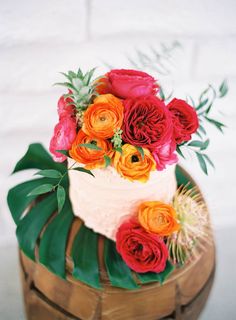 a white cake with red and orange flowers on top is sitting on a wooden stand