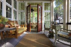 the sun shines through two large windows onto an enclosed porch with seating and potted plants